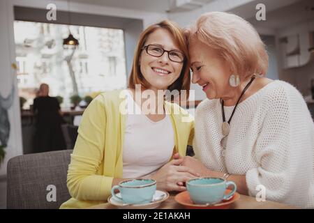 Bonne femme mûre souriant joyeusement à la caméra, en câlin avec sa mère âgée. Une femme âgée riant, tenant les mains avec sa fille d'âge moyen Banque D'Images