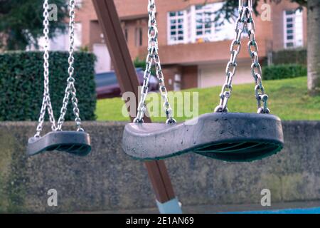 Balancer à vide sur l'aire de jeux après la pluie. Sièges en plastique noir avec gouttes de pluie et chaînes métalliques. Concept de solitude. Vue spectaculaire Banque D'Images