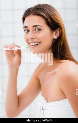 bonne femme souriant à l'appareil photo tout en tenant la brosse à dents dans la salle de bains Banque D'Images