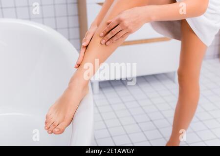 coupe courte pour femme appliquant une lotion pour le corps sur la jambe salle de bains Banque D'Images