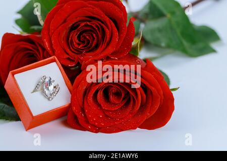 Anneau dans la boîte rouge et belles roses rouges sur fond blanc. Concept de la Saint-Valentin. Banque D'Images