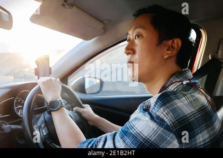 Gros plan du jeune homme asiatique qui regarde la route urbaine en conduisant une voiture en ville Banque D'Images
