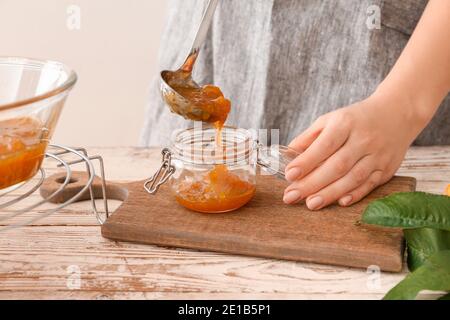 Femme versant de la confiture de pêche savoureuse dans un pot Banque D'Images