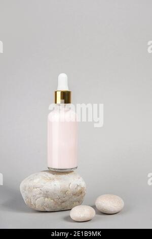 Collagène anti-âge rose, sérum facial en flacon en verre transparent avec pipette en or et pierres naturelles sur fond gris. Cosmet de spa biologique naturel Banque D'Images