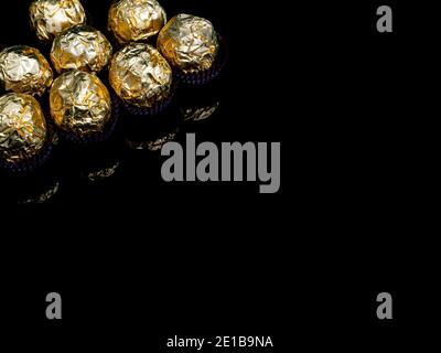 Bonbons au chocolat ronds dans un emballage doré sur fond noir. Bonbons ronds. Couleur dorée. Un cadeau de vacances. Anniversaire. Photo de nourriture. Mets sucrés. Happ Banque D'Images