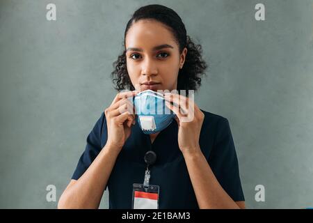 Infirmière afro-américaine tenant un masque de protection regardant la caméra au mur Banque D'Images