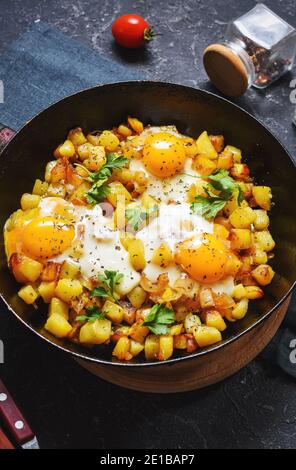 Pommes de terre hachées avec des œufs et des herbes pour le petit déjeuner sur un arrière-plan en pierre noire Banque D'Images