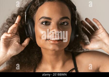 Passion d'une musique jeune fille afro-américaine à l'écoute de son favori musique dansant avec les mains levées dans les écouteurs portant le dessus noir isolé sur Banque D'Images