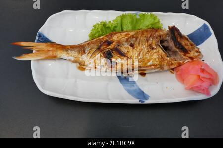 Bream grillé à fines nageoires ornées avec sauce soja et rouge gingembre mariné dans une plaque de céramique carrée blanche sur noir arrière-plan Banque D'Images