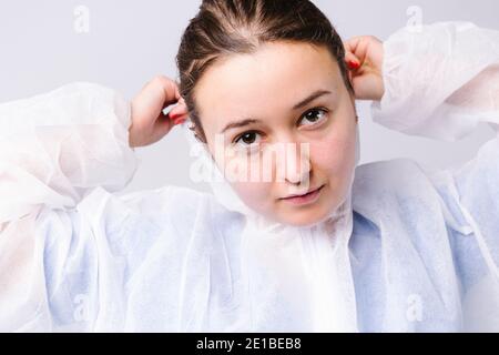 Adorable femme médecin met sur une robe de protection sur un fond blanc. Photo agrandie. Le concept de lutte contre le virus. Banque D'Images