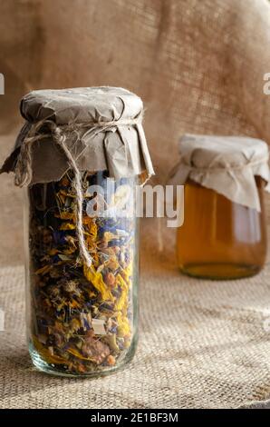 Herbes médicinales et médecine alternative concept.Herbal herbes séchées médicinales et miel d'abeille. Thé de fleur séché et miel liquide cru dans des pots en verre sur toile de jute. Banque D'Images