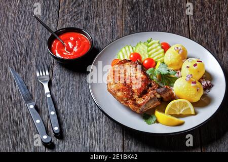 karbonade de porc rôtie, côtelettes de porc avec pomme de terre bouillie et tranches de concombre et de citron sur une assiette sur une table en bois, vue horizontale d'en haut Banque D'Images