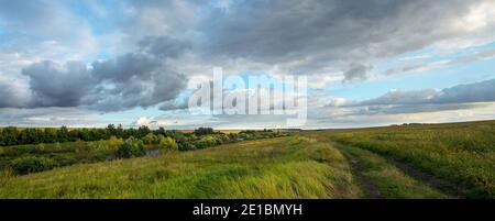 Paysage panoramique d'été avec route rurale et nuages noirs de pluie sur les champs de la ferme Banque D'Images