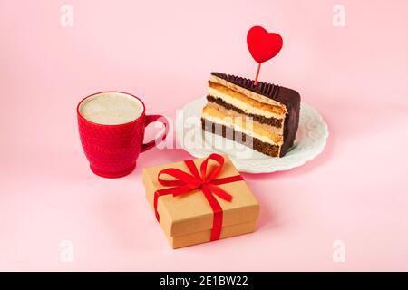 Cappuccino dans une tasse rouge, gâteau et cadeau dans une boîte sur fond rose. Concept d'amour, Saint Valentin. Banque D'Images