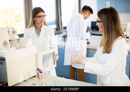 Jeunes femmes scientifiques dans un flacon de mise en blouse de laboratoire blanc avec un échantillon pour une analyse sur un système d'ionchromatographie en laboratoire biomédical Banque D'Images