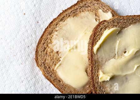 Vue rapprochée en hauteur de deux tranches de pain de blé légèrement grillé avec margarine sur des essuie-tout en papier blanc à la lumière naturelle. Banque D'Images