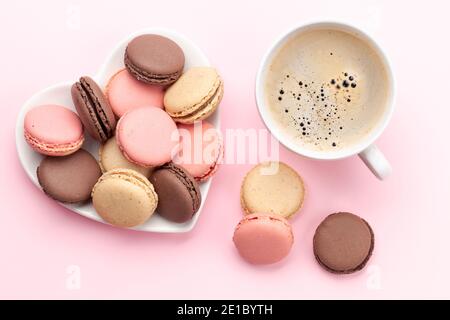 Saint-Valentin avec macarons dans une assiette en forme de coeur et une tasse de café sur fond rose. Plan d'étapage avec vue de dessus Banque D'Images