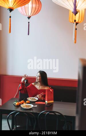 Belle jeune femme asiatique vêtue de vêtements rouges mangeant de la nourriture asiatique dans un restaurant chinois vietnamien de fête lanternes en papier colorées, célébrant le nouveau chinois Banque D'Images