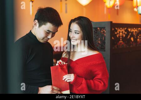 Beau jeune couple asiatique en vêtements rouges donner présent dans le restaurant chinois vietnamien festif avec des lanternes en papier coloré, célébrant la ne chinoise Banque D'Images