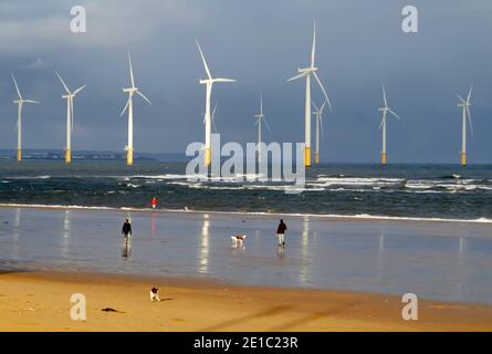 Trois personnes faisant de l'exercice sur la plage lors d'une journée hivernale ensoleillée à Coatham, Cleveland, Royaume-Uni, avec quelques-unes des éoliennes Redcar derrière Banque D'Images