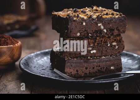 Gros plan de brownies au caramel et aux noix au chocolat noir garniture empilée sur une assiette noire Banque D'Images