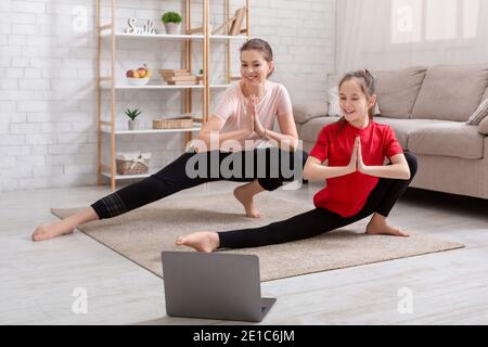 Bonne mère millénaire et sa fille adolescente regardant le tutoriel vidéo de sports en ligne, faisant des exercices sur le sol à la maison Banque D'Images