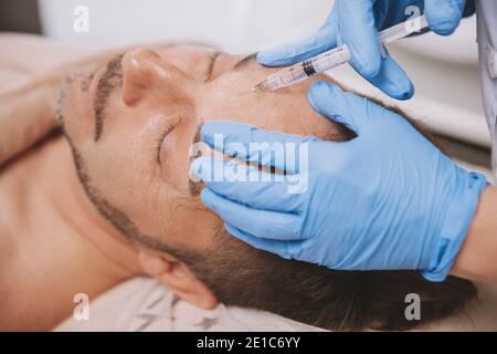 Homme mature recevant des injections de remplissage facial par un cosmétologue professionnel. Homme d'âge moyen qui reçoit un traitement anti-rides au salon de beauté. Botox, dispo Banque D'Images