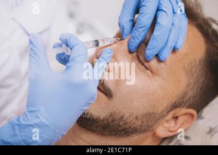 Gros plan d'une esthéticienne professionnelle effectuant un travail de nez non chirurgical sur un client mâle mature. Un homme barbu obtient un travail de nez non chirurgical Banque D'Images