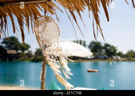 En regardant le ciel bleu et les rayons du soleil à travers un parapluie de plage de paille et des perles suspendues de plumes et de fils. Magnifique arrière-groun abstrait d'été Banque D'Images