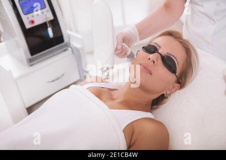 Belle femme mature recevant un traitement de beauté laser à la clinique de cosmétologie. Esthéticienne éliminant la décoloration de la peau d'un patient Banque D'Images