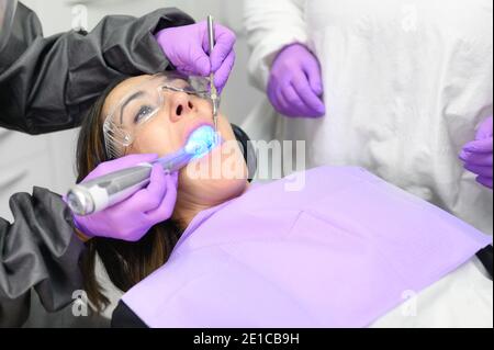 Jeune femme recevant une procédure de lumière ultraviolette au cabinet de dentiste. Photo de haute qualité Banque D'Images