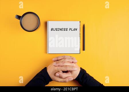 Les mains d'un homme d'affaires avec un ordinateur portable en spirale avec des idées de plan d'affaires prêtes à être écrites dans lui. Arrière-plan jaune avec espace de copie. Banque D'Images