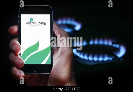 Un homme qui regarde l'application pour la compagnie d'énergie Atlantic Énergie sur son téléphone devant sa cuisinière à gaz (usage éditorial uniquement) Banque D'Images