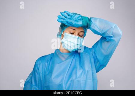 Un médecin épuisé en robe de protection tient la main à la tête. Travail et fatigue pendant une pandémie de covid. Banque D'Images