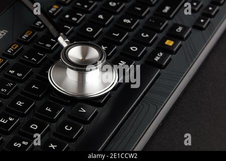 Stéthoscope sur clavier d'ordinateur noir. Service de réparation informatique ou concept de soins de santé en ligne Banque D'Images