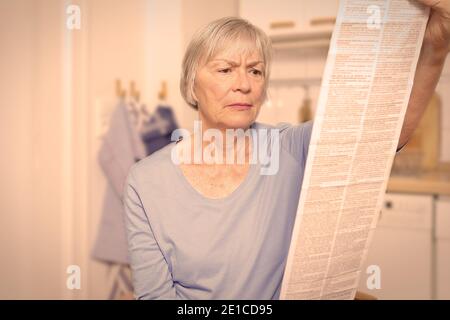 Femme âgée réfléchie avec une très longue notice de médicament pour son médicament prescrit, effet filtre. Banque D'Images