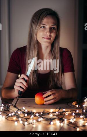 une jeune femme blonde tient un couteau dans sa main et se prépare à couper une pomme. Les traditions et les mauvaises habitudes d'un européen en célébrant Noël. À partir de g Banque D'Images