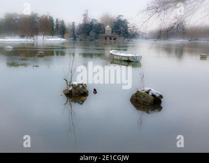 Bateau couvert de neige dans le lac et Temple de l'amour à l'arrière-plan. Lac Daumesnil (forêt de Vincennes, Paris, France). Mise au point douce et angles blanchis. Banque D'Images