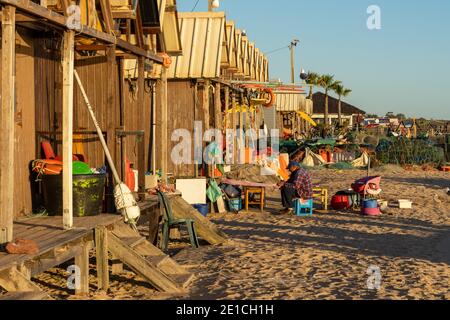 Amaraco da Pera, Portugal - 30 décembre 2020 : fiserman assis à l'extérieur de sa hutte au coucher du soleil et en train de réparer ses filets Banque D'Images