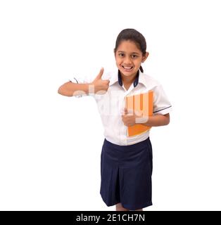 Portrait d'une jeune fille indienne heureuse portant un uniforme souriant et montrant le pouce vers le haut le geste de la main et représentant la victoire. Banque D'Images