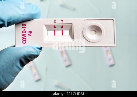 La main du médecin dans un gant bleu contient un test COVID-19 express cassette avec le résultat positif par rapport aux autres cassettes de test sur l'arrière-plan est flou Banque D'Images