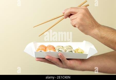 Homme tenant un sushi dans une assiette jetable et mangeant de la nourriture japonaise par des baguettes. Concept de plats à emporter Banque D'Images