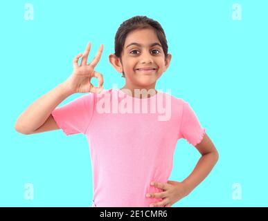 Portrait d'une petite fille indienne mignonne sur fond bleu montrant le signe de forme 'parfaite ' avec les mains et exprimant la satisfaction et l'appréciation. Banque D'Images