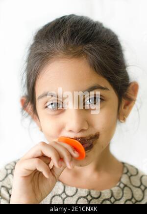 Petite fille indienne souriante aime manger un bâton de glace avec des taches autour de sa bouche. Banque D'Images