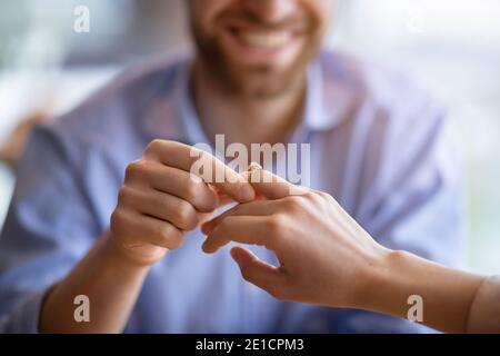 Un homme heureux tenant la main de son fiancé, en mettant l'anneau d'engagement sur son doigt, vue rapprochée Banque D'Images