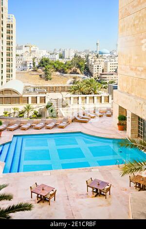 La terrasse sur le toit de la piscine du Grand Hyatt Amman, en Jordanie. Chaises longues et table et chaises pour dîner avec le roi Abdullah I Mosquée et Amman paysage urbain dans le loin. Banque D'Images