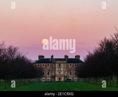 Pleine lune s'élevant dans le ciel rose au-dessus de la maison d'Archerfield House ou manoir, East Lothian, Écosse, Royaume-Uni Banque D'Images