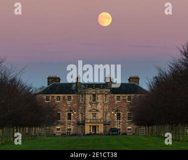 Pleine lune s'élevant dans le ciel rose au-dessus de la maison d'Archerfield House ou manoir, East Lothian, Écosse, Royaume-Uni Banque D'Images