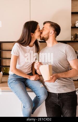 Embrasser un jeune couple a un bon moment ensemble à la maison tout en mangeant la nourriture chinoise Banque D'Images