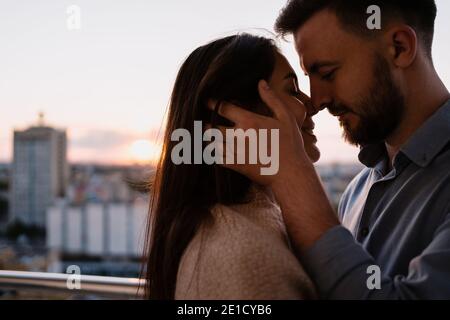 Gros plan portrait, homme et femme souriant les uns aux autres au coucher du soleil avec la ville en arrière-plan. Couple romantique moments intimes Banque D'Images